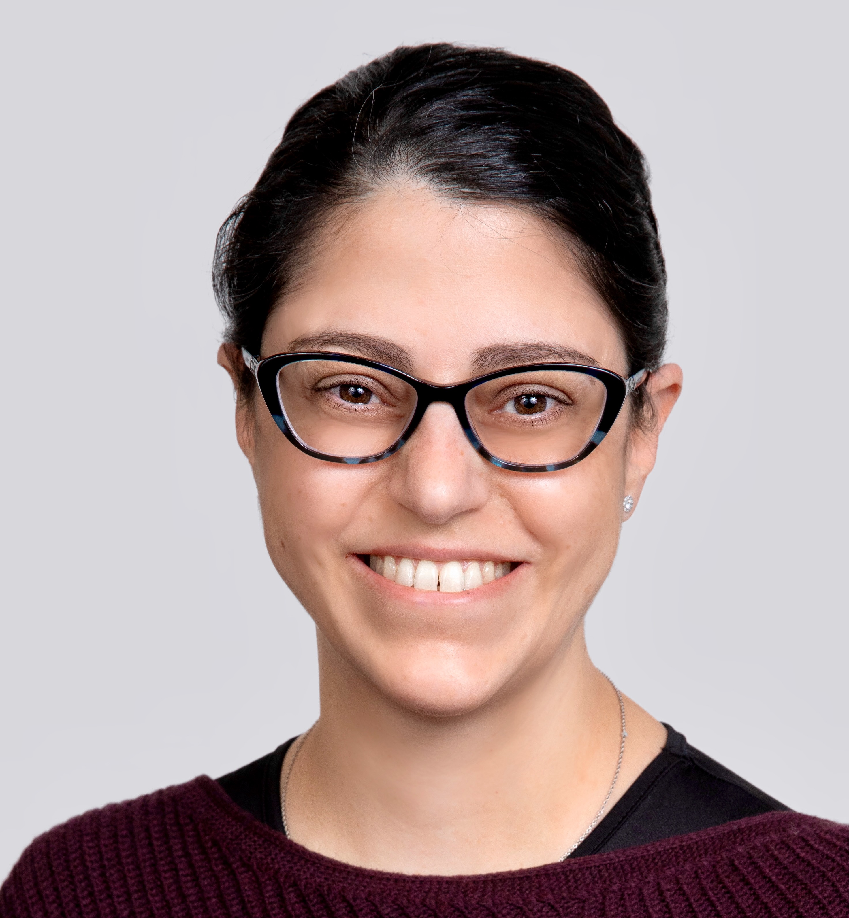 Woman smiling with glasses and dark hair pulled back in red top.