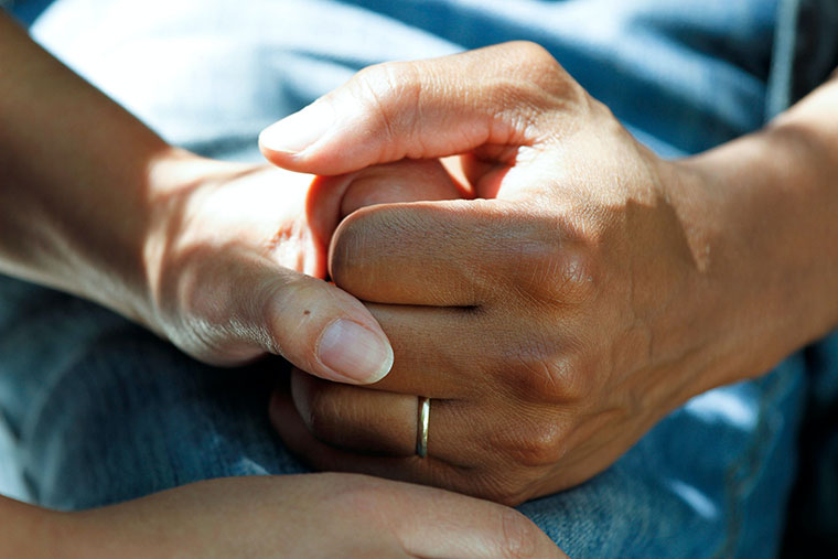 Two hands holding each other in foreground with blue jean in background.