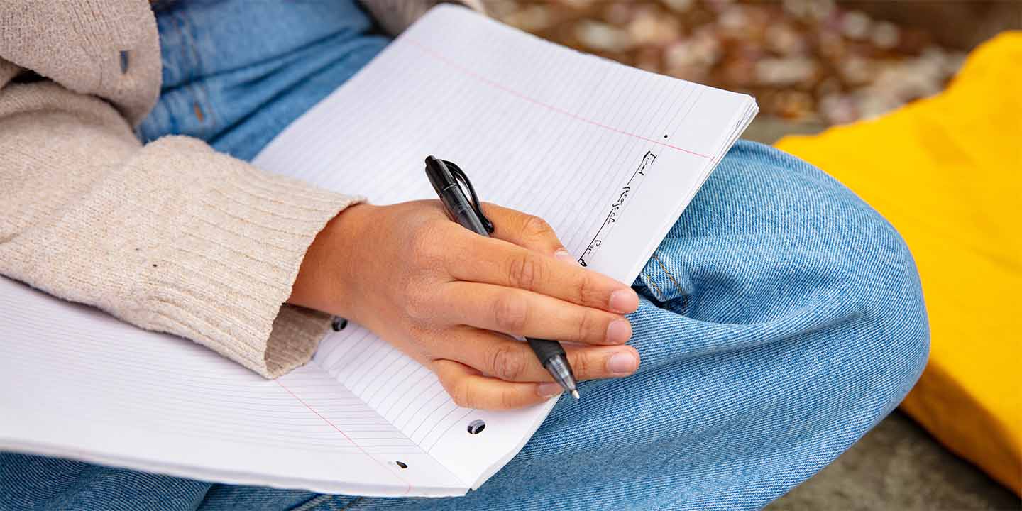 Close up of a student’s hand holding a pen and a journal